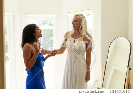 Bride and bridesmaid laughing together, holding hands in bright room Bride and bridesmaid laughing together, holding hands in bright room 135631613