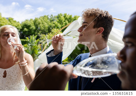 Guests enjoying champagne outdoors at wedding celebration, smiling and toasting Guests enjoying champagne outdoors at wedding celebration, smiling and toasting 135631615