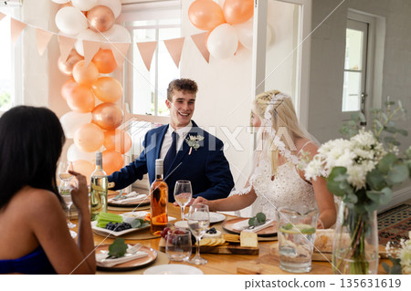 Bride and groom smiling at table with friends during wedding celebration 135631619