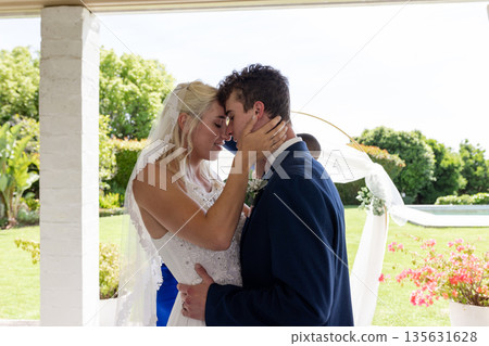 Embracing lovingly, bride and groom in outdoor wedding ceremony surrounded by nature Embracing lovingly, bride and groom in outdoor wedding ceremony surrounded by nature 135631628