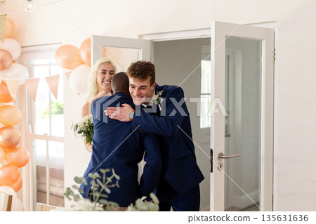 Groom hugging friend at wedding reception, both smiling joyfully in celebration 135631636