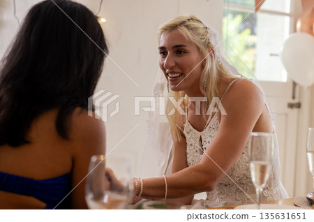 Bride in white dress joyfully chatting with guest at wedding reception Bride in white dress joyfully chatting with guest at wedding reception 135631651