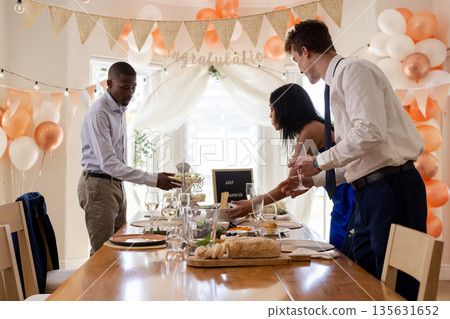Friends celebrating wedding at home, setting table with food and drinks Friends celebrating wedding at home, setting table with food and drinks 135631652