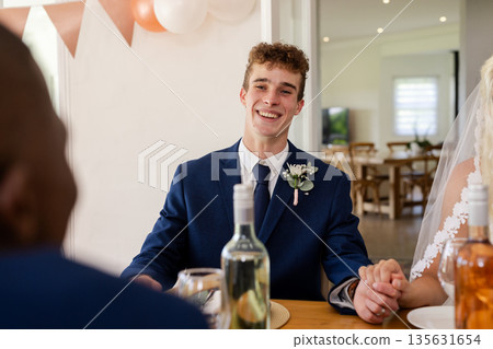 Groom in blue suit smiling while holding hands during wedding celebration 135631654