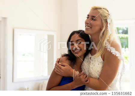 Bride and friend embracing joyfully in bright room during wedding celebration 135631662