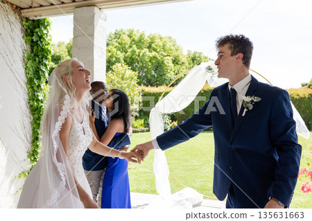 Bride and groom joyfully dancing outdoors, celebrating wedding with friends 135631663