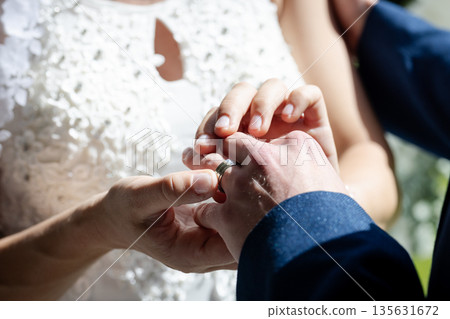 Bride placing ring on groom's finger during wedding ceremony, hands close-up 135631672