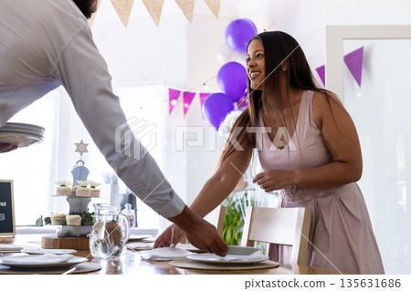 Smiling woman setting table for bar mitzvah with festive decorations Smiling woman setting table for bar mitzvah with festive decorations 135631686