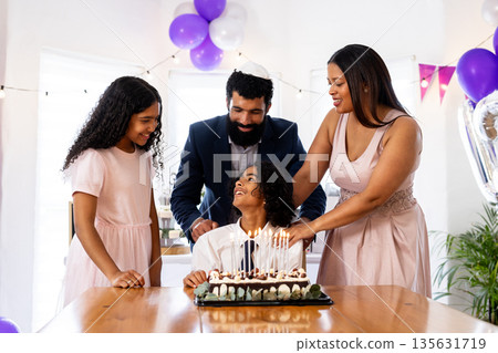 Family celebrating birthday with cake and candles, smiling and enjoying together Family celebrating birthday with cake and candles, smiling and enjoying together 135631719