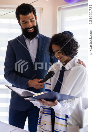 At bar mitzvah, boy reading from torah during ceremony, father holding microphone At bar mitzvah, boy reading from torah during ceremony, father holding microphone 135631721