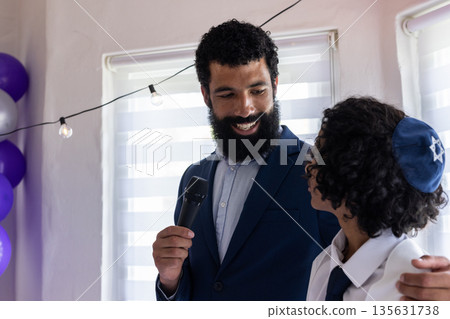 Man holding microphone smiling at boy wearing kippah during bar mitzvah 135631738