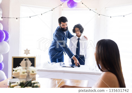 Father and son in suits speaking at family celebration, sharing joyful moment 135631742