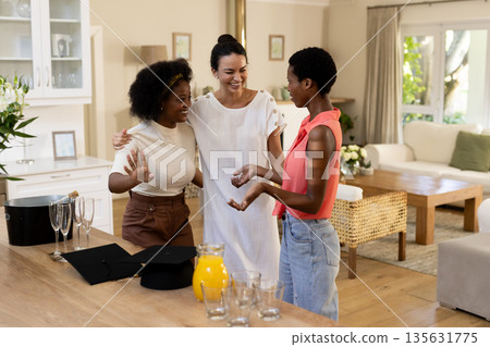 Celebrating graduation, diverse female friends laughing together in cozy living room Celebrating graduation, diverse female friends laughing together in cozy living room 135631775