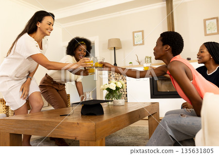 Women toasting with drinks around coffee table, enjoying time together at home 135631805