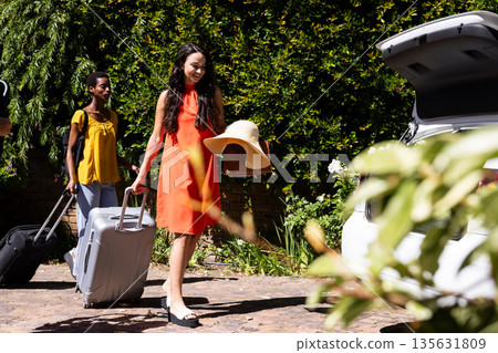 Friends packing car with luggage for road trip, smiling and enjoying sunny day Friends packing car with luggage for road trip, smiling and enjoying sunny day 135631809