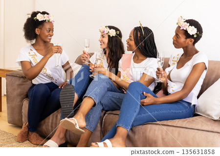 Celebrating friendship, diverse women toasting with champagne on cozy couch 135631858