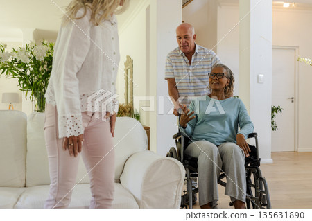Senior friends enjoying conversation at home, one woman in wheelchair smiling warmly 135631890