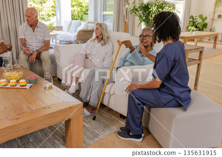 Senior friends enjoying conversation with caregiver in cozy living room setting Senior friends enjoying conversation with caregiver in cozy living room setting 135631915