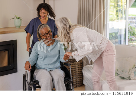 Caregiver assisting senior woman in wheelchair while friend visits at home 135631919