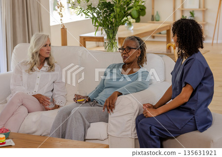 Senior friends relaxing on sofa, enjoying conversation with healthcare professional Senior friends relaxing on sofa, enjoying conversation with healthcare professional 135631921