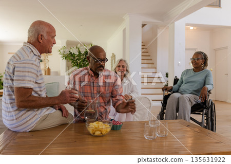 Senior friends enjoying snacks and conversation together in cozy living room 135631922