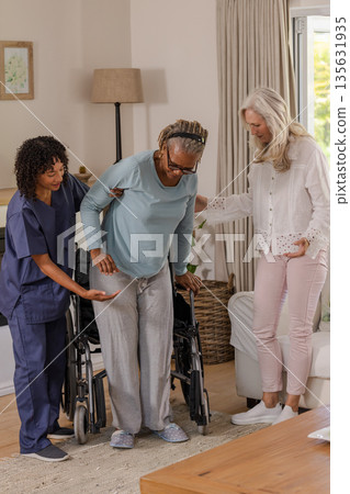 Caregiver and friend assisting senior man standing from wheelchair at home 135631935