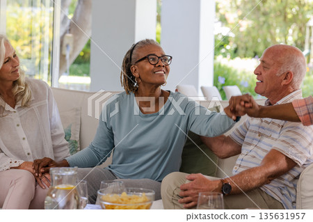 Senior friends laughing and enjoying conversation together in cozy living room Senior friends laughing and enjoying conversation together in cozy living room 135631957