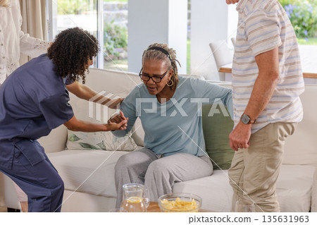 Caregiver assisting senior African American woman standing up from sofa at home Caregiver assisting senior African American woman standing up from sofa at home 135631963