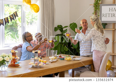Celebrating retirement, senior friends with drinks and snacks, smiling together at home 135631974