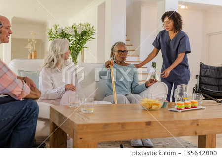 Senior friends enjoying conversation at home with caregiver offering support Senior friends enjoying conversation at home with caregiver offering support 135632000