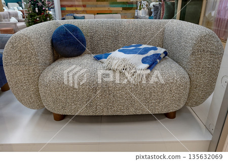 A curved sofa with a blue pillow and a blanket is shown inside a furniture store. The setting has colorful furniture in the background 135632069
