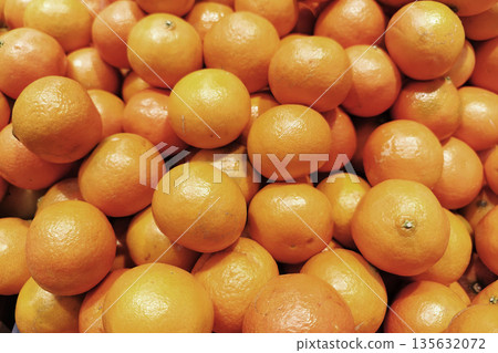 Fresh mandarins are piled high in a market. Shoppers are browsing the selection of fruits. The scene shows vibrant oranges during the day Fresh mandarins are piled high in a market. Shoppers are browsing the selection of fruits. The scene shows vibrant oranges during the day 135632072