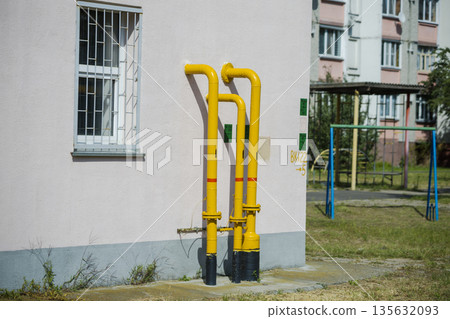 Yellow pipes run along the exterior wall of a building next to a playground with equipment. Sunlight shines on the scene during midday Yellow pipes run along the exterior wall of a building next to a playground with equipment. Sunlight shines on the scene during midday 135632093