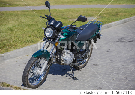 A motorcycle is parked on a paved surface along a grassy area in an outdoor setting during the day with no clouds in the sky 135632118