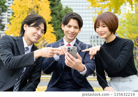 Three Japanese men and women looking at their smartphones in an office district Three Japanese men and women looking at their smartphones in an office district 135632219
