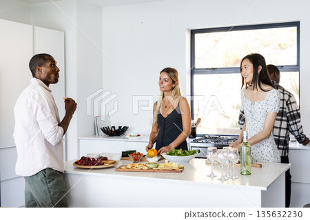 In kitchen, friends preparing food and chatting while gathering around counter In kitchen, friends preparing food and chatting while gathering around counter 135632230