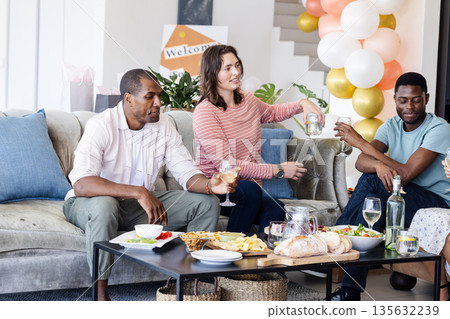 Friends enjoying drinks and snacks at home during casual celebration gathering Friends enjoying drinks and snacks at home during casual celebration gathering 135632239