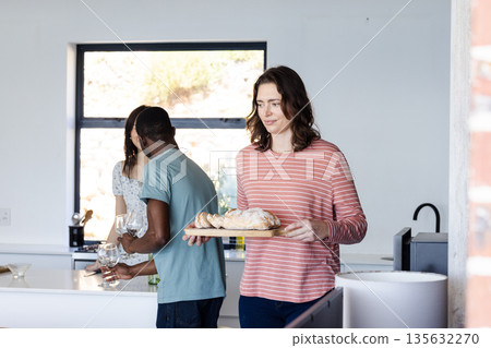 Friends preparing meal together in kitchen, carrying bread and setting table 135632270
