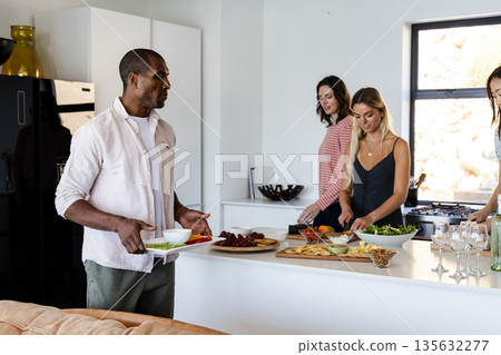 African American man serving food while friends prepare dishes in modern kitchen African American man serving food while friends prepare dishes in modern kitchen 135632277