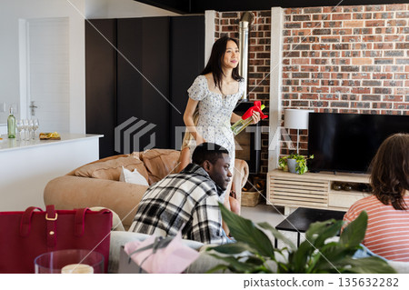 Woman holding wine bottle smiling at friends during cozy home gathering 135632282