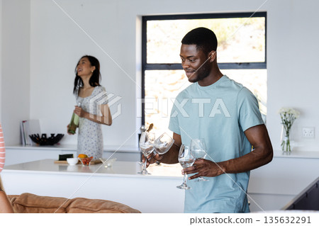 Friends preparing drinks and laughing together in modern kitchen during celebration 135632291