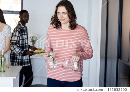 Woman carrying water and glasses at home during casual gathering with friends 135632300