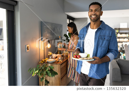 African American man carrying snacks while woman prepares drinks at home gathering African American man carrying snacks while woman prepares drinks at home gathering 135632320