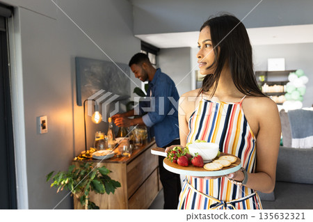 Woman holding appetizer plate while man prepares drinks at home celebration 135632321