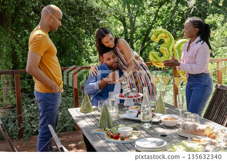 Celebrating birthday outdoors, friends enjoying cake and holding golden balloons 135632340