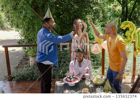 Friends celebrating birthday outdoors, wearing party hats and giving high fives Friends celebrating birthday outdoors, wearing party hats and giving high fives 135632374