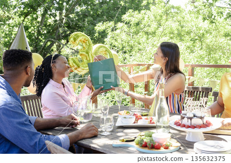 Celebrating outdoors, friends exchanging gifts at birthday party with joyful smiles 135632375