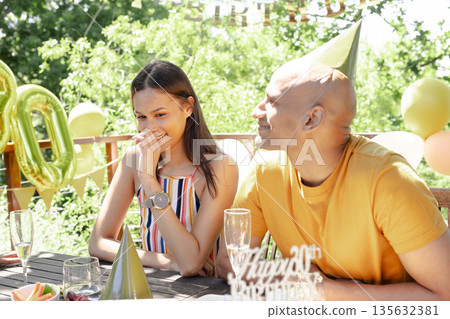 Celebrating birthday outdoors, friends enjoying party with balloons and party hats Celebrating birthday outdoors, friends enjoying party with balloons and party hats 135632381