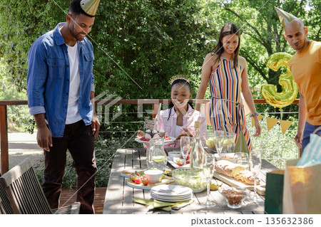 Friends celebrating birthday outdoors with food and drinks, wearing party hats 135632386