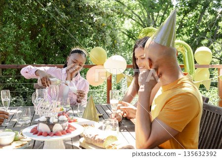 Friends celebrating outdoors, pouring drinks and enjoying cake with party hats Friends celebrating outdoors, pouring drinks and enjoying cake with party hats 135632392